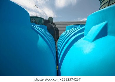 Plastic tanks from kits for building household sewage treatment plants. Blue and black large barrels (tanks) from kits for self-assembly of small domestic sewage treatment plants stored by a tin fence