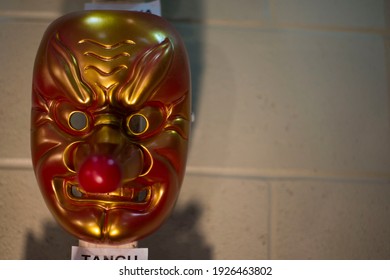 A plastic tengu mask against a cinderblock wall