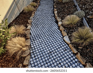 Plastic tiles with perforations and locks are suitable for building roads and parking lots. Stones line a permeable gravel path in a garden with perennials and mulching bark on a slope