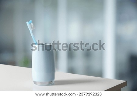Plastic toothbrush in holder on white table against blurred background, space for text