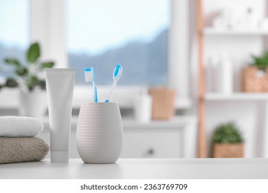 Plastic toothbrushes in holder, toothpaste and towels on white table indoors. Space for text