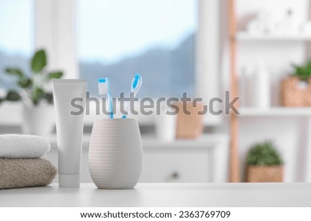 Plastic toothbrushes in holder, toothpaste and towels on white table indoors. Space for text