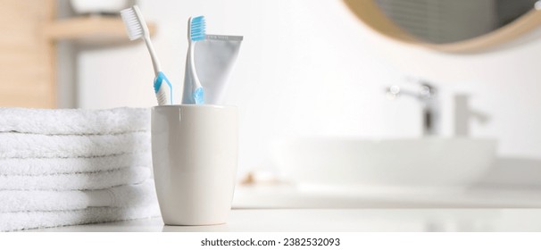 Plastic toothbrushes, toothpaste and towels on white table in bathroom, space for text. Banner design