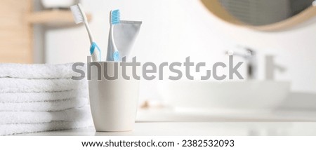 Plastic toothbrushes, toothpaste and towels on white table in bathroom, space for text. Banner design
