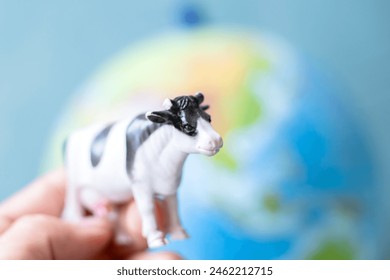 Plastic toy cow in front of world model background. Cows breeding and CO2 emission idea concept. Cattle farming. Methane emissions from livestock. Animal. Horizontal photo. No people, nobody. 
