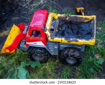 Plastic Toy Dump Truck Bucket Loader With Submerged Earth Standing On The Ground.