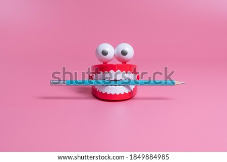 A plastic toy in the form of red jaws with white teeth and eyes holds a pencil between its teeth. Copywriting concept