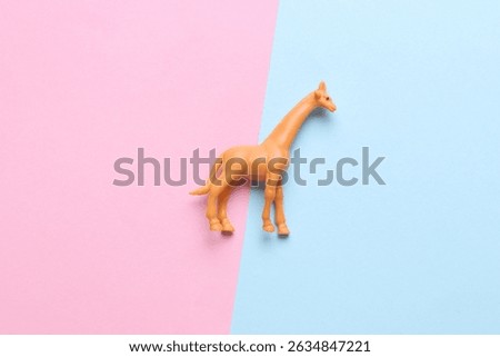 Plastic toy giraffe figurine on blue pink background