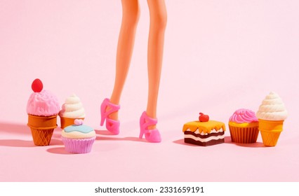 Plastic toy legs with high heels and little sweets on pastel pink background. Minimal art pink poster.