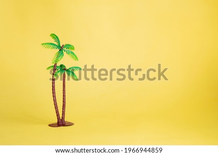 Plastic toy palm tree on yellow background with copy space. Postcard from travels to tropical countries.