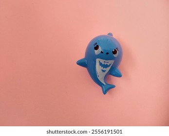 A plastic toy in the shape of a blue shark on a pale red background - Powered by Shutterstock