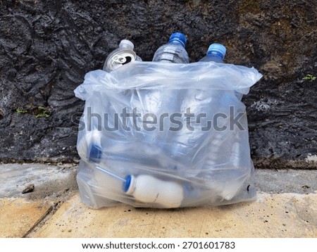 Plastic trash bag filled with empty plastic bottles and aluminum cans against a concrete wall, symbolizing waste management, recycling, and environmental pollution awareness.
