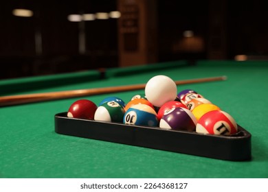 Plastic triangle rack with billiard balls and cue on green table indoors, space for text