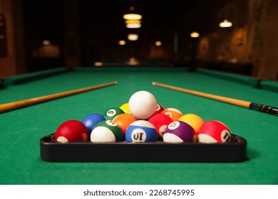 Plastic triangle rack with billiard balls and cues on green table indoors, space for text