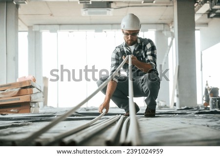 Plastic tubes in hands. Construction worker in uniform in empty unfinished room.