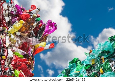 Plastic waste from used crumpled PET bottles in colored bales on blue sky background with white cloud. Closeup of empty crushed beverage packagings pressed in green or red packages. Garbage recycling.