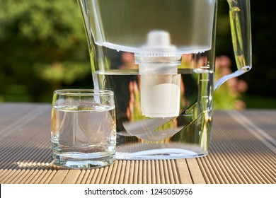 Plastic Water Filtration Pitcher And A Clean Glass Of A Clear Water Close Up On The Summer Garden Background                              