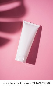Plastic white tube for cream or lotion. Skin care or sunscreen cosmetic in top view on pink background with palm leaves shadow. Beauty concept for face care