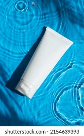 Plastic White Tube For Cream Or Lotion On Beautiful Burst And Glare. Skincare Or Sunscreen Cosmetic On Blue Background. Beauty Concept For Face Care. Natural Sunlight And Water Spills. Summer Mood.