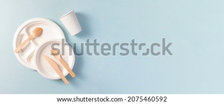 Plastic-free disposable tableware, horizontal banner format with copy space. Paper plate, food containers, glass, wooden spoon, fork, knife. Single-use dinnerware non-plastic alternatives