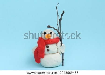 Plasticine snowman with pepper eyes and twig broom isolated on lightblue background.