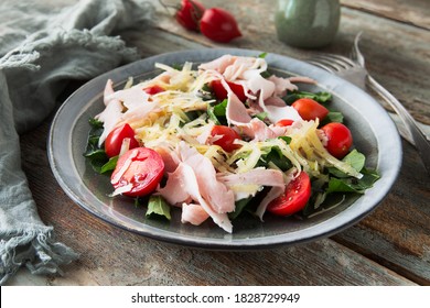 plate with arugula salad, ham, cheese and cherry tomatoes on a wooden table close-up, shallow depth of field - Powered by Shutterstock