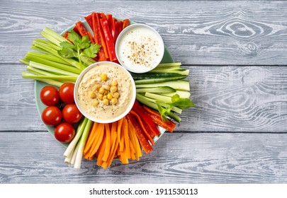 Plate Of Assorted Colorful Fresh Vegetable Sticks With Hummus And Yogurt Dips On Light Blue Background. Top View. Healthy Raw Vegetarian Food Enriched With Vitamins And Microelements