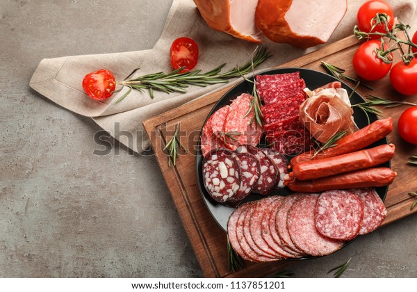 Plate with assortment of delicious deli meats\
on grey background