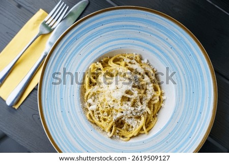 A plate of authentic Italian cacio e pepe pasta, featuring al dente spaghetti coated with Pecorino Romano cheese and freshly ground black pepper. The dish is served in a blue-striped ceramic bowl.