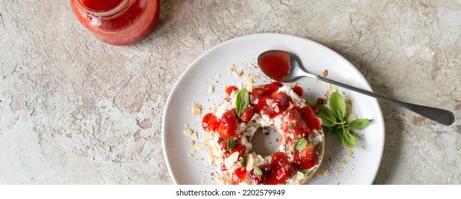 A Plate With A Bagel With Mascarpone, Strawberries And Basil On A Light Table