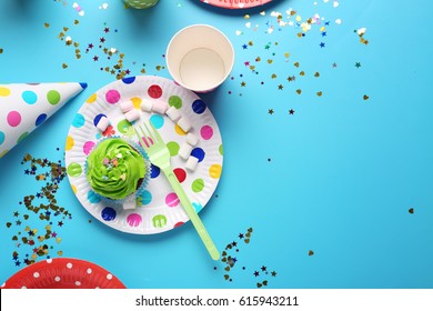 Plate with birthday cupcake and paper glass on table