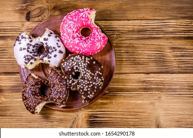 Plate With Bitten Glazed Donuts On Wooden Table. Top View