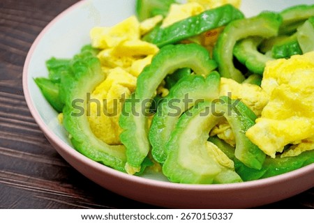 A plate of bitter melon scrambled eggs in the background of a wooden table