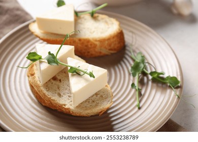 Plate with bread, triangles of tasty processed cheese and micro green on light table, closeup