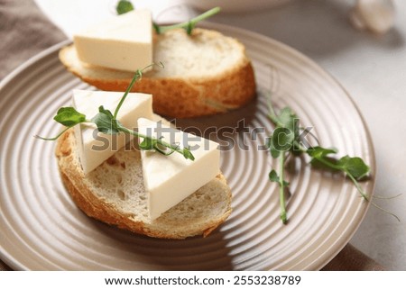 Plate with bread, triangles of tasty processed cheese and micro green on light table, closeup