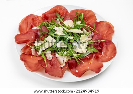 Plate of bresaola with rocket and parmesan in close-up on a white background. Typical Italian food.