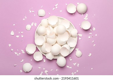 Plate with broken egg shells on lilac background