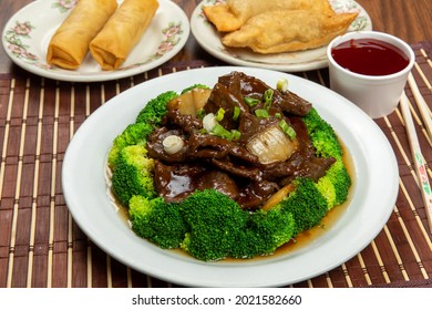 A Plate Of Chinese Beef And Broccoli With Plates Of Egg Rolls And Spring Rolls In The Background