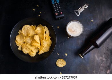 Plate Of Chips, Remote Control TV, Beer, Bottle Opener Top View Of A Dark Metal Table.