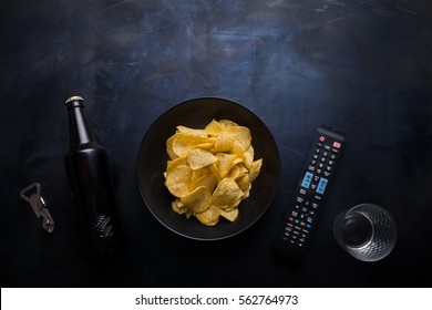 Plate Of Chips, Remote Control TV, Beer, Empty Glass Bottle Opener Top View Of A Dark Metal Table. Free Time. Relaxation At Tv.