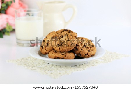 Plate with chocolate chip cookies and glass of milk on white background