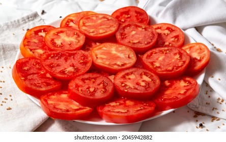 Plate With Chopped Tomatoes. Tomato Slices Lie In Two Layers, You Can See The Cut And Seeds. The Plate Stands On Light Towels With Folds. Side View Of The Finished Dish Of Fresh Vegetables.