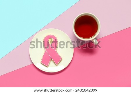Plate with cookie in shape of pink ribbon and cup of tea on color background. Breast cancer awareness concept