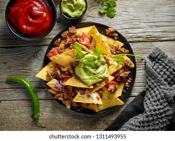 plate of corn chips nachos with fried minced meat and guacamole on wooden kitchen table, top view