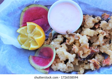 A Plate Of Cracked Conch With Dipping Sauce And Garnishes