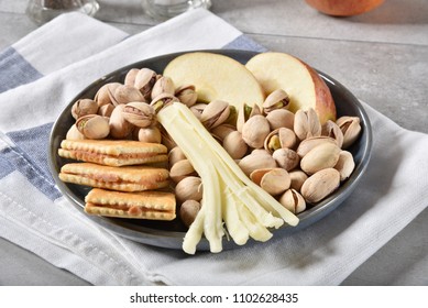 A Plate Of Crackers With Peanut Butter, Pistachios, String Cheese And Sliced Apples