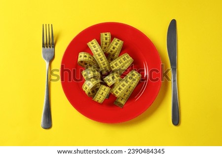 Plate, cutlery and measuring tape on yellow background, flat lay. Diet concept