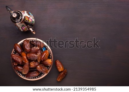 Plate with dates, coffee pot  on dark brown wooden table. Ramadan background.  Top view.