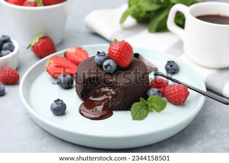 Plate with delicious chocolate fondant, berries and mint on grey table, closeup