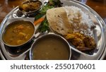 A plate of delicious Dal Bhat with chicken curry, crackers, curry sauce, and some vegetables